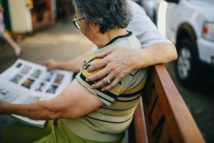 Grandmother sitting on a bench, looking at a photo album, highlighting family tensions. Grandmother sitting on a bench, looking at a photo album, highlighting family tensions.