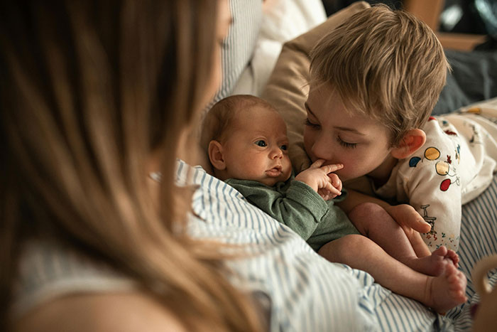 Mother holding baby with young sibling nearby, highlighting family tension dynamics. Mother holding baby with young sibling nearby, highlighting family tension dynamics.