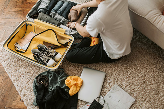 A person packing a suitcase with clothes and shoes on a carpeted floor. A person packing a suitcase with clothes and shoes on a carpeted floor.
