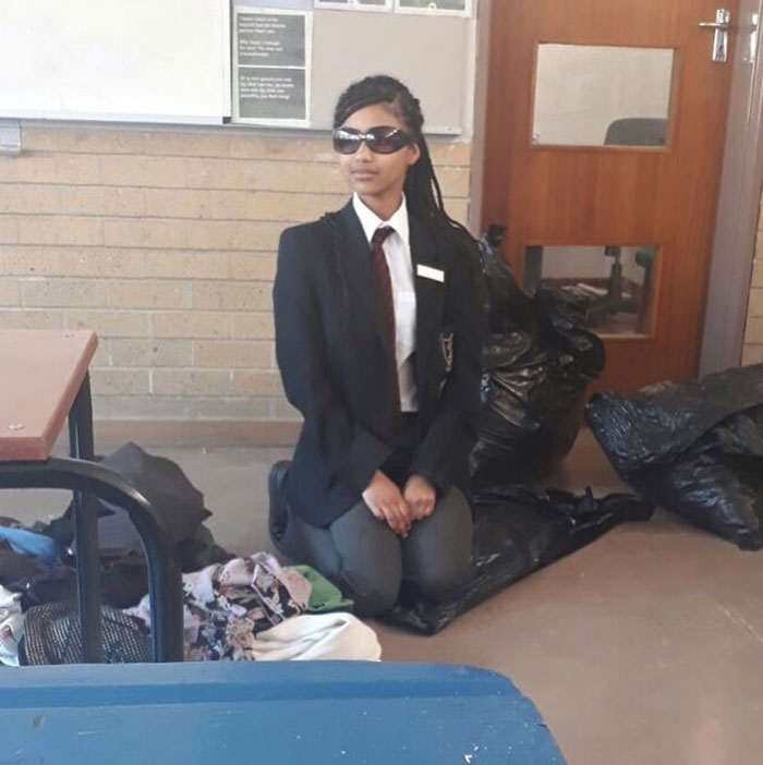Tyla during her school years, wearing a formal uniform with a blazer, tie, and sunglasses, kneeling in a classroom near black garbage bags and folded clothes. The setting appears casual yet formal, with a classroom door and bulletin board in the background. Tyla during her school years, wearing a formal uniform with a blazer, tie, and sunglasses, kneeling in a classroom near black garbage bags and folded clothes. The setting appears casual yet formal, with a classroom door and bulletin board in the background.