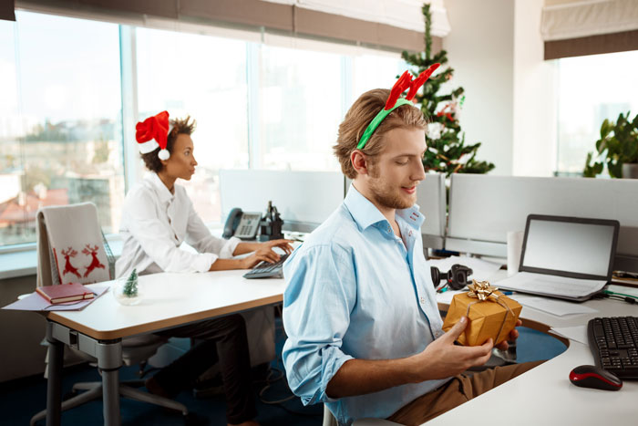 Office employees with holiday headbands, holding a gift at their desks. Office employees with holiday headbands, holding a gift at their desks.