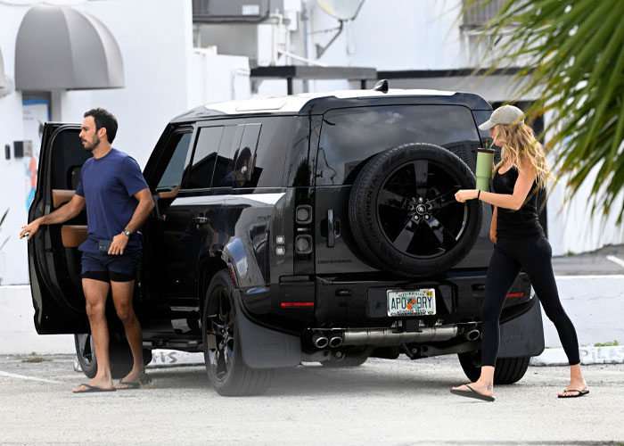 A black SUV parked in a lot with a man in casual attire getting out and a woman wearing athletic wear and a cap walking nearby, holding a tumbler. A black SUV parked in a lot with a man in casual attire getting out and a woman wearing athletic wear and a cap walking nearby, holding a tumbler.