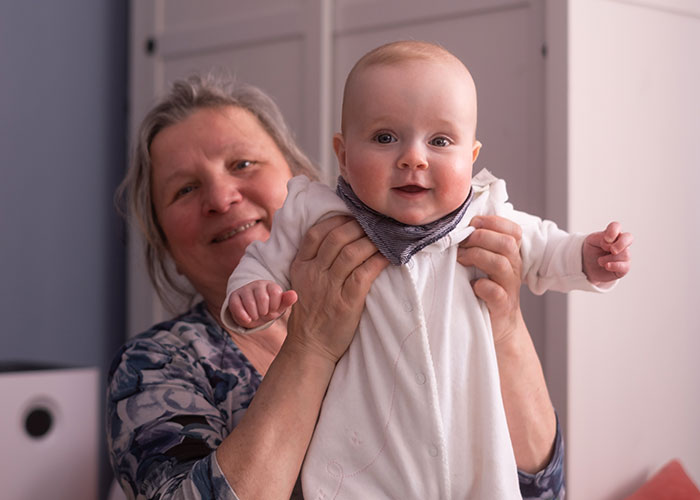 Grandmother happily holding a smiling baby in a white onesie indoors. Grandmother happily holding a smiling baby in a white onesie indoors.