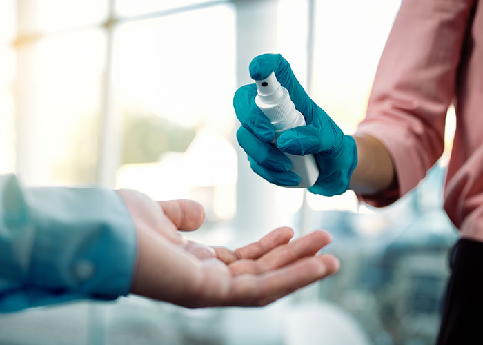 Hand sanitizer being sprayed onto an outstretched palm by a gloved hand in a bright setting. Hand sanitizer being sprayed onto an outstretched palm by a gloved hand in a bright setting.
