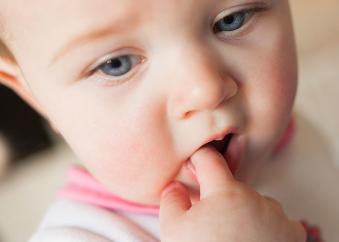 Close-up of a baby with blue eyes gently touching their lip. Close-up of a baby with blue eyes gently touching their lip.