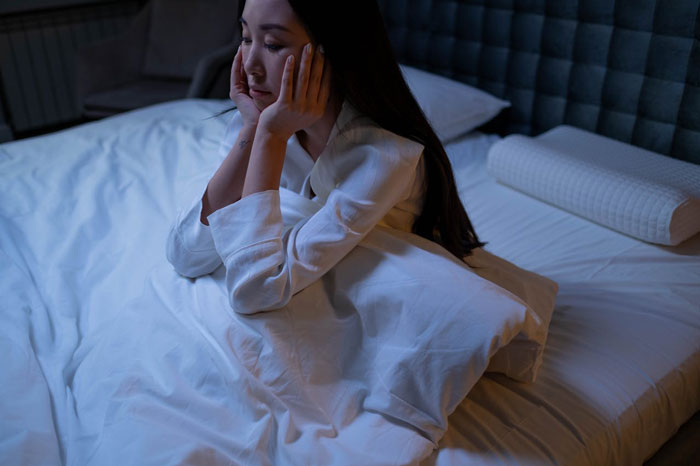 Woman in bed appearing stressed, struggling with insomnia due to loud roommates and nightly disturbances. Woman in bed appearing stressed, struggling with insomnia due to loud roommates and nightly disturbances.