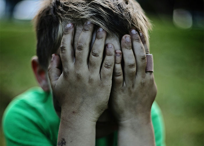 Child in distress with hands over face, green shirt, showing emotional struggle. Child in distress with hands over face, green shirt, showing emotional struggle.