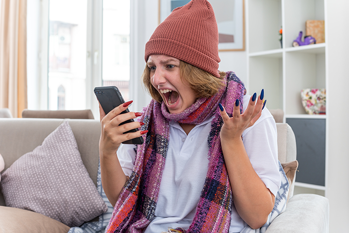 Woman in beanie and scarf looking surprised while using a smartphone on a couch, indoors. Woman in beanie and scarf looking surprised while using a smartphone on a couch, indoors.