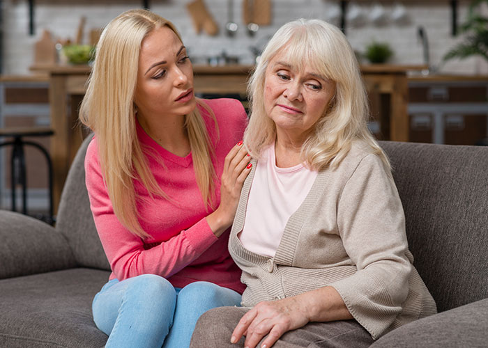 Daughter comforting concerned mother-in-law on a couch, expressing support and empathy. Daughter comforting concerned mother-in-law on a couch, expressing support and empathy.