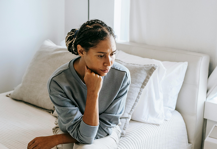 Woman sitting on a bed, looking thoughtful, highlighting dream wedding concerns. Woman sitting on a bed, looking thoughtful, highlighting dream wedding concerns.