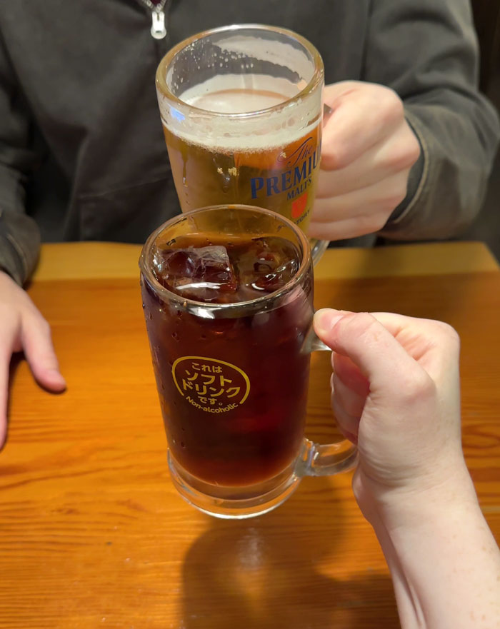 People clinking glasses in Japan, highlighting work rules with drinks on a wooden table. People clinking glasses in Japan, highlighting work rules with drinks on a wooden table.