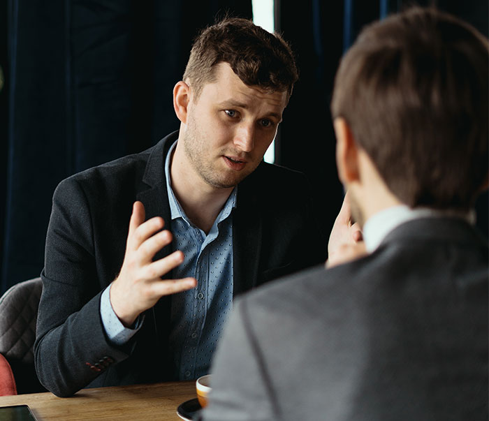 Man in a suit discussing company lunch policy with a colleague in an office setting. Man in a suit discussing company lunch policy with a colleague in an office setting.
