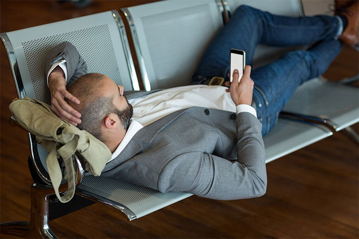 Man in a gray suit relaxing on an office bench, holding a phone, illustrating a potential employee scenario. Man in a gray suit relaxing on an office bench, holding a phone, illustrating a potential employee scenario.