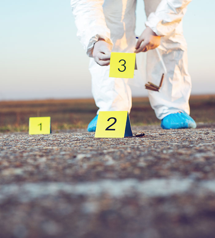 Forensic investigator in white suit examining evidence markers on the ground. Forensic investigator in white suit examining evidence markers on the ground.