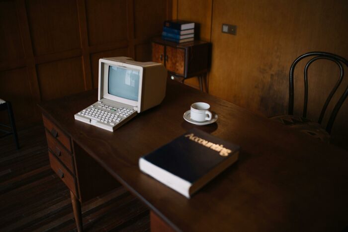 Vintage computer on a desk with a book, evoking 2000s teen nostalgia.