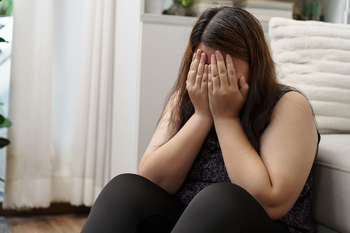 A woman sitting on the floor with her face in her hands, expressing emotions related to body image and being plus-size. A woman sitting on the floor with her face in her hands, expressing emotions related to body image and being plus-size.