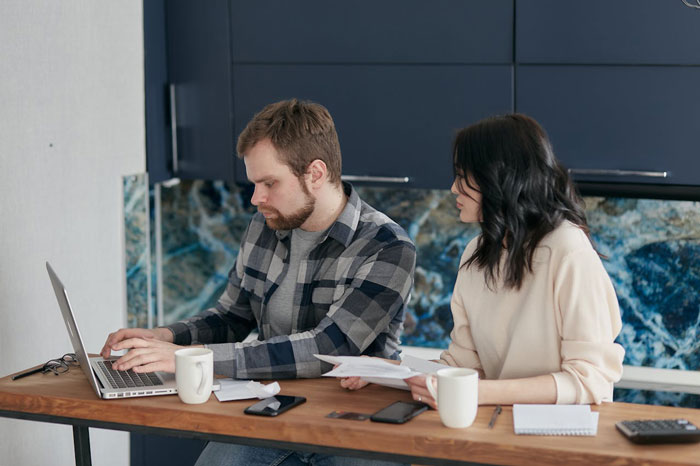Two people at a table, one on a laptop, discussing a topic related to revenge, with coffee cups and papers. Two people at a table, one on a laptop, discussing a topic related to revenge, with coffee cups and papers.