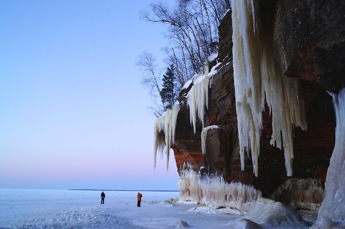Amazing views with ice formations and two people exploring a frozen landscape beneath towering cliffs.