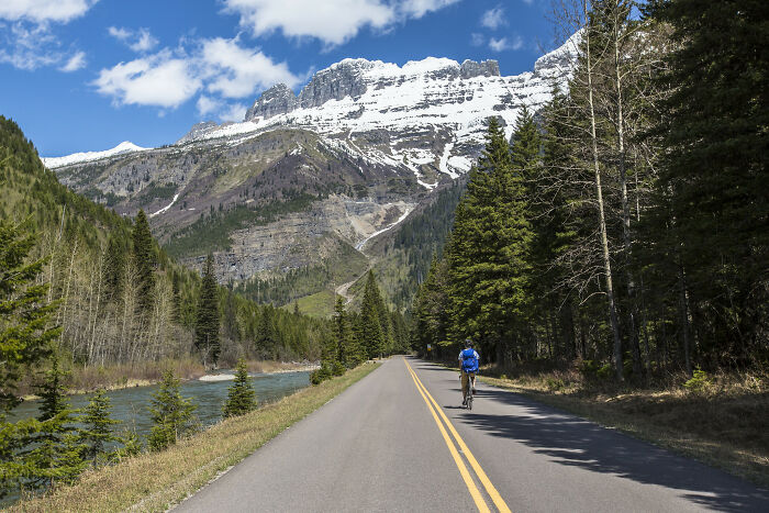 Cyclist on a scenic road with mountains and trees, showcasing amazing views in a natural setting.