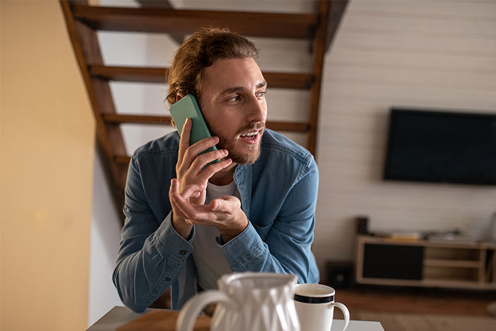 Man in blue shirt talking on phone, discussing last-minute party cancellation at home. Man in blue shirt talking on phone, discussing last-minute party cancellation at home.