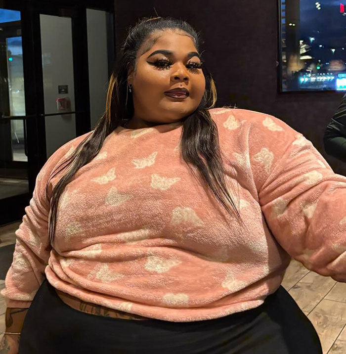 Plus size woman in a pink sweater with butterfly patterns, sitting indoors. Plus size woman in a pink sweater with butterfly patterns, sitting indoors.