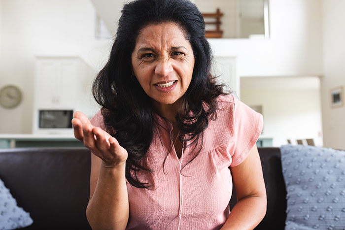 A woman in a pink shirt looking frustrated in a living room, relating to family and wealth issues. A woman in a pink shirt looking frustrated in a living room, relating to family and wealth issues.