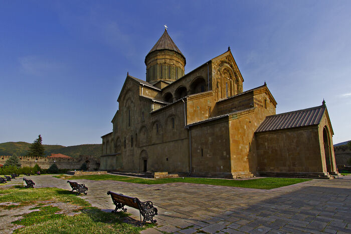 Ancient stone church with a conical roof under a clear blue sky, showcasing fascinating church architecture.