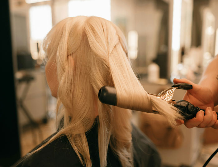 Woman having her hair styled with a curling iron in a salon setting. Woman having her hair styled with a curling iron in a salon setting.