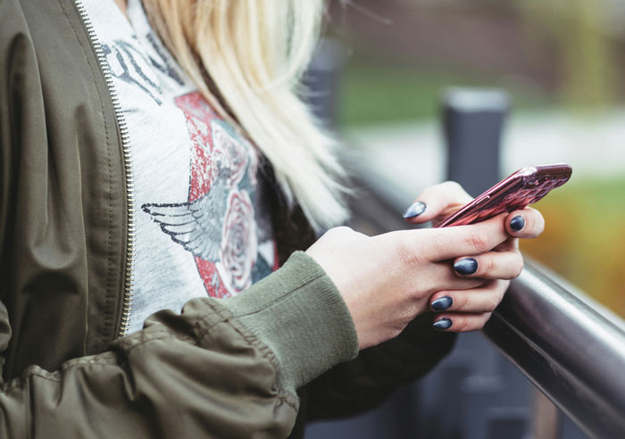Woman using a smartphone outdoors, wearing a green jacket and graphic tee, prioritizing financial responsibility. Woman using a smartphone outdoors, wearing a green jacket and graphic tee, prioritizing financial responsibility.