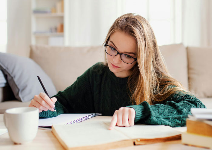 Teen girl with glasses studying, wearing a green sweater, writing in a book. Teen girl with glasses studying, wearing a green sweater, writing in a book.