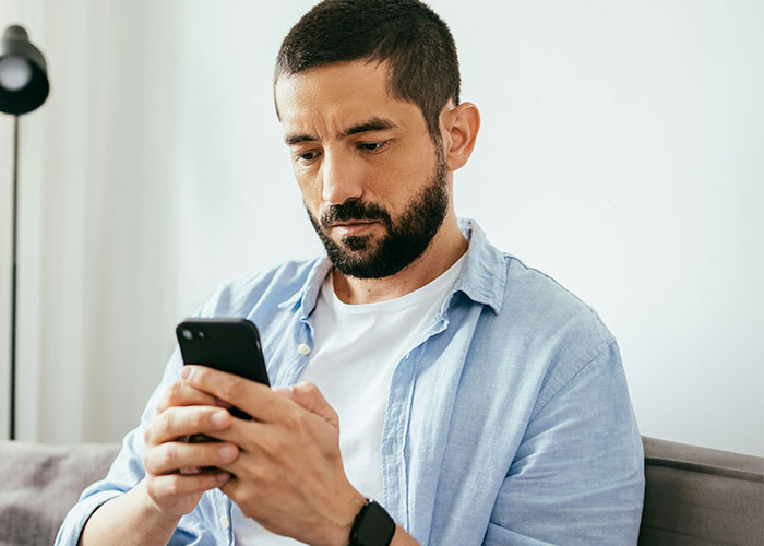Man in a light blue shirt looking at his phone, appearing thoughtful. Man in a light blue shirt looking at his phone, appearing thoughtful.