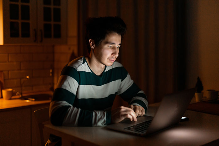 Man in striped shirt using laptop alone at night, symbolic of friend group deception. Man in striped shirt using laptop alone at night, symbolic of friend group deception.