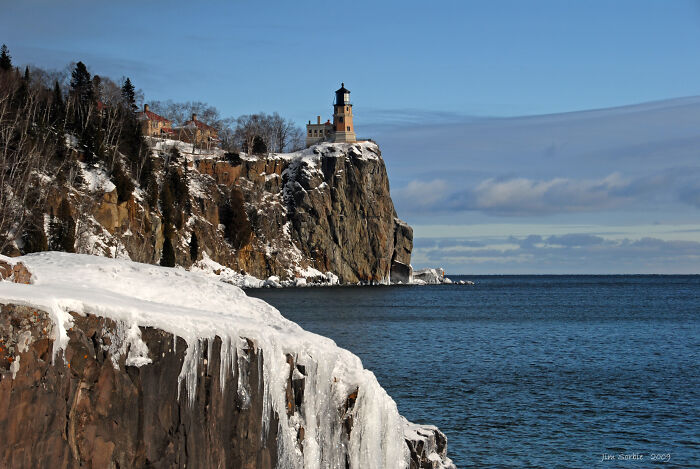 Lighthouse perched on a snowy cliff overlooking the ocean, showcasing amazing views in a northern state.