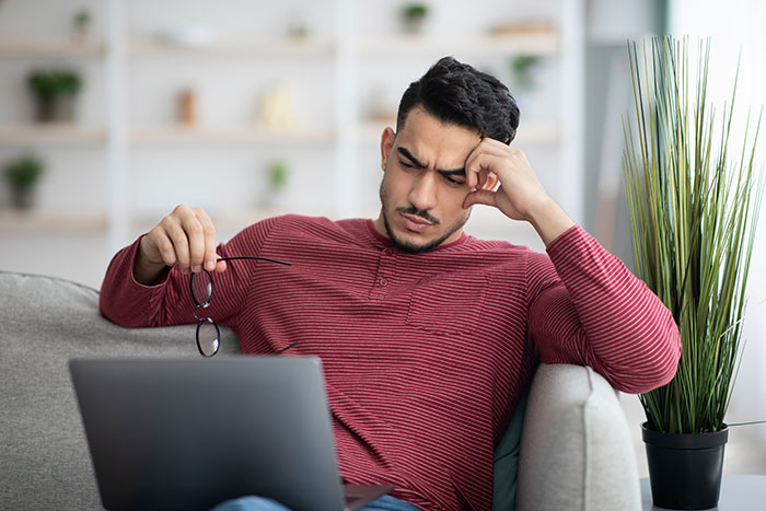 Man frustrated over apartment scam, holding glasses, looking at laptop in living room. Man frustrated over apartment scam, holding glasses, looking at laptop in living room.