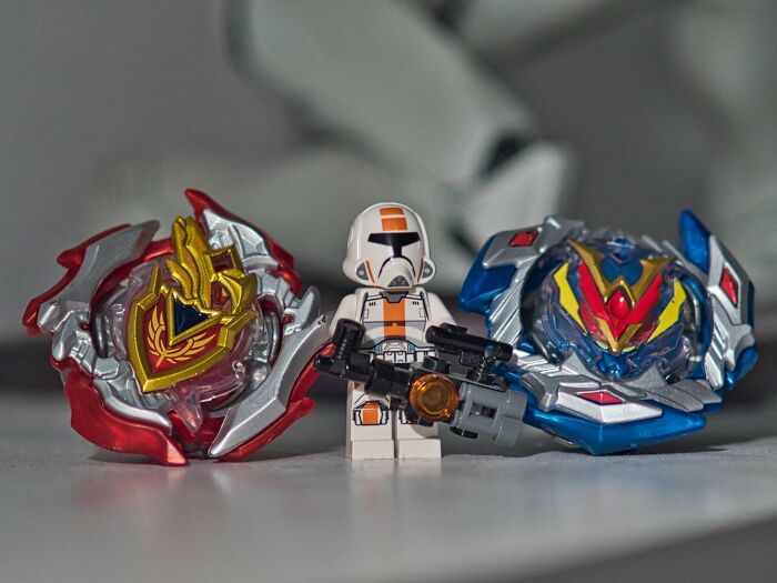 2000s nostalgia: action figure with blaster between two colorful spinning tops on a table.