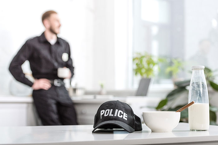 Police cap on a table with milk and cereal, officer in background, related to apartment scam incident. Police cap on a table with milk and cereal, officer in background, related to apartment scam incident.
