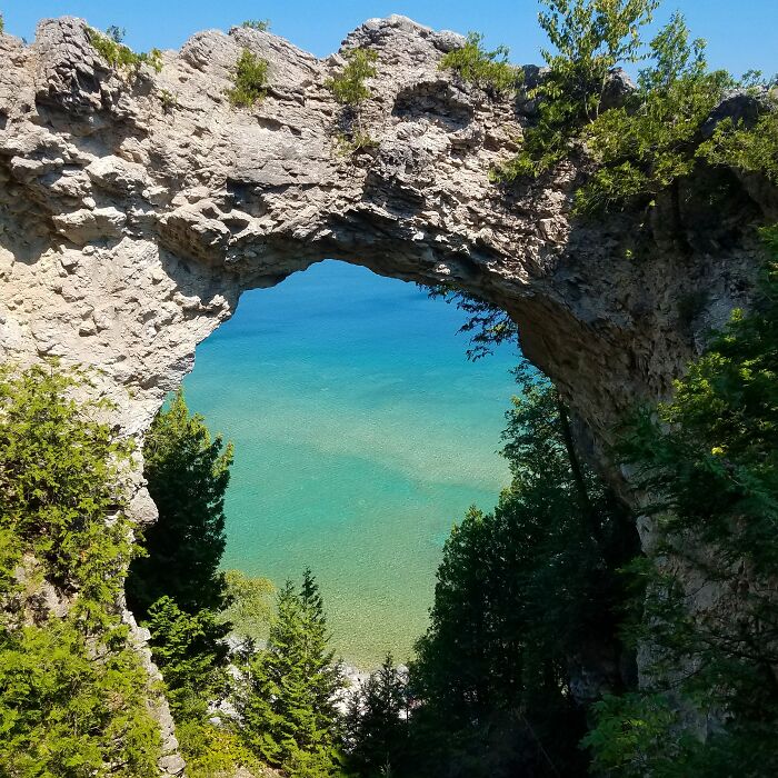 Natural rock arch framing vibrant lake scenery, showcasing amazing views in a lush state park setting.