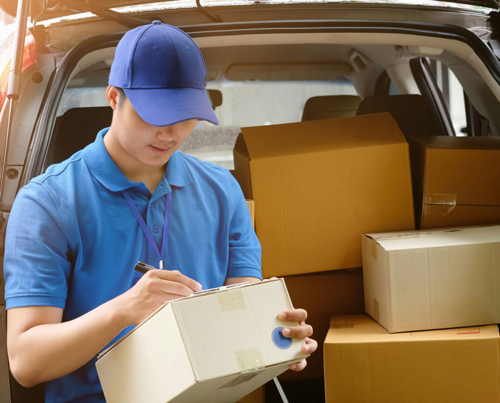 Amazon driver wearing a blue uniform writing a note beside delivery boxes in a vehicle. Amazon driver wearing a blue uniform writing a note beside delivery boxes in a vehicle.