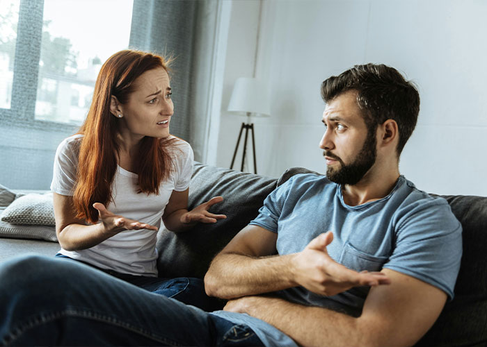 Man and woman in a heated discussion on a couch, both gesturing with their hands. Man and woman in a heated discussion on a couch, both gesturing with their hands.