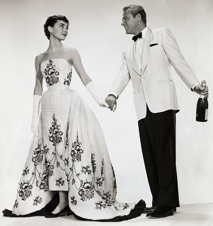 A woman in an elegant, embroidered gown and gloves holds hands with a man in a tuxedo, exuding elegance and class. A woman in an elegant, embroidered gown and gloves holds hands with a man in a tuxedo, exuding elegance and class.