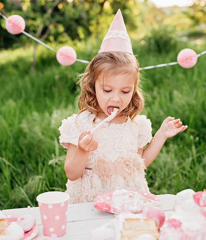 A child at a pink-themed party eating dessert, wearing a pink party hat. A child at a pink-themed party eating dessert, wearing a pink party hat.