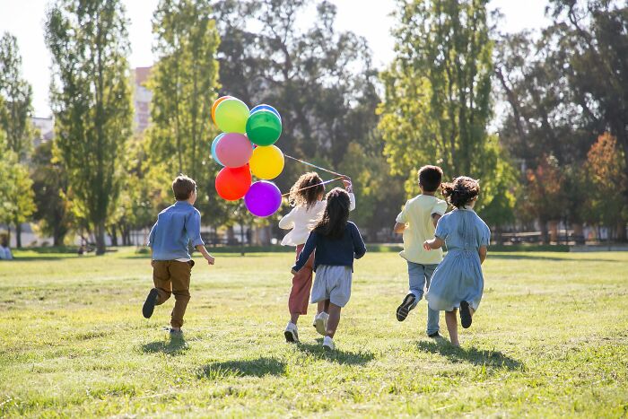 Teens in the 2000s running with colorful balloons in a sunny park.