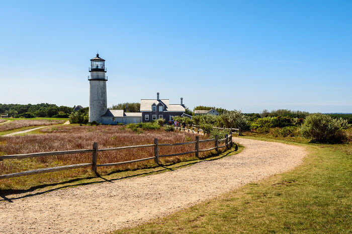 Lighthouse by scenic coastal path under clear blue sky, offering amazing views in rural state setting.