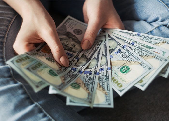 Person holding several hundred-dollar bills, illustrating finance and income combining for married couples. Person holding several hundred-dollar bills, illustrating finance and income combining for married couples.