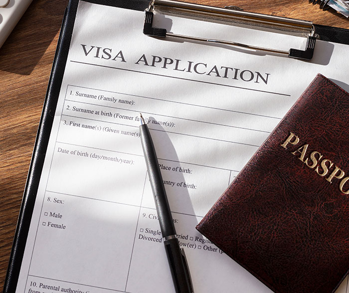 “Visa application form and passport on a wooden desk, symbolizing international travel or documentation process.” “Visa application form and passport on a wooden desk, symbolizing international travel or documentation process.”