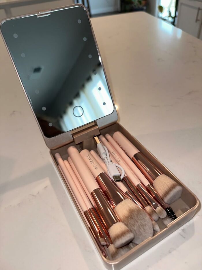 Travel-ready compact makeup kit with brushes, mirror, and charging cable on a countertop.