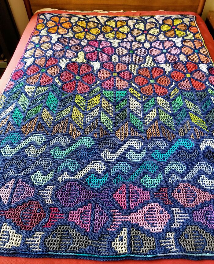 Colorful crocheted blanket with flowers, leaves, waves, and fish patterns, showcasing a proud crochet enthusiast’s creative project.