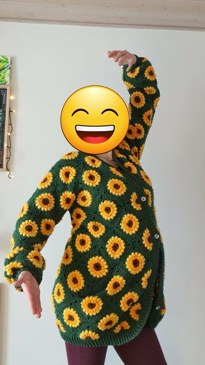 Person posing in a sunflower-patterned crochet cardigan, showcasing their proud handmade crochet project indoors.