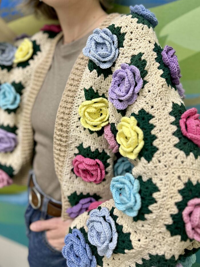 Close-up of a colorful crochet cardigan featuring 3D flower appliques worn by a person proudly showcasing their crochet project.