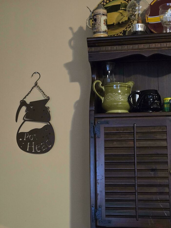 Confusing perspectives: shadow casts a profile of a person on the wall next to a shelf with various decorative items. Confusing perspectives: shadow casts a profile of a person on the wall next to a shelf with various decorative items.